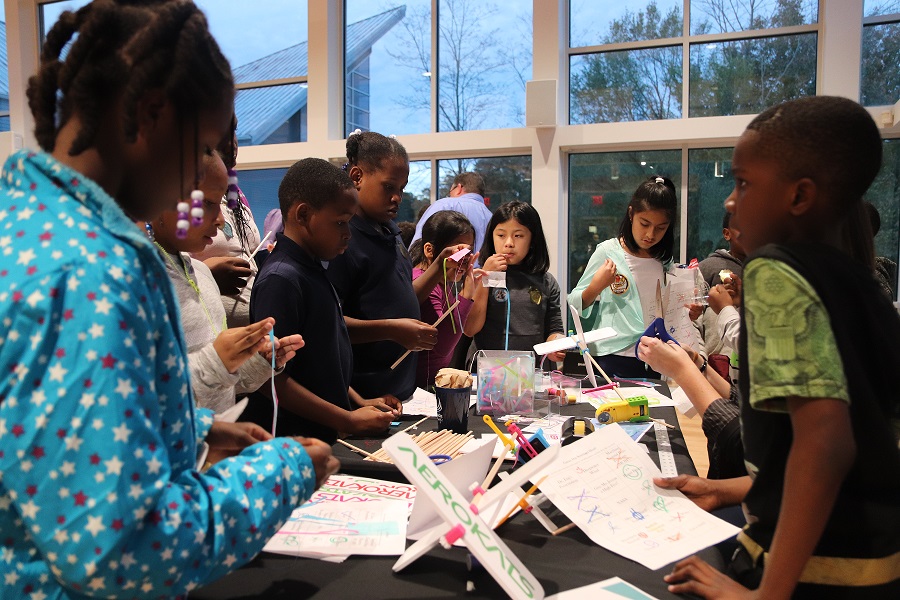A group of young students surrounding a table in different stages of assembling mini kites