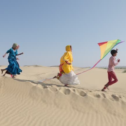 Group of happy Indian children running across sand dune with colorful kite - desert village, Thar Desert, Rajasthan, India.