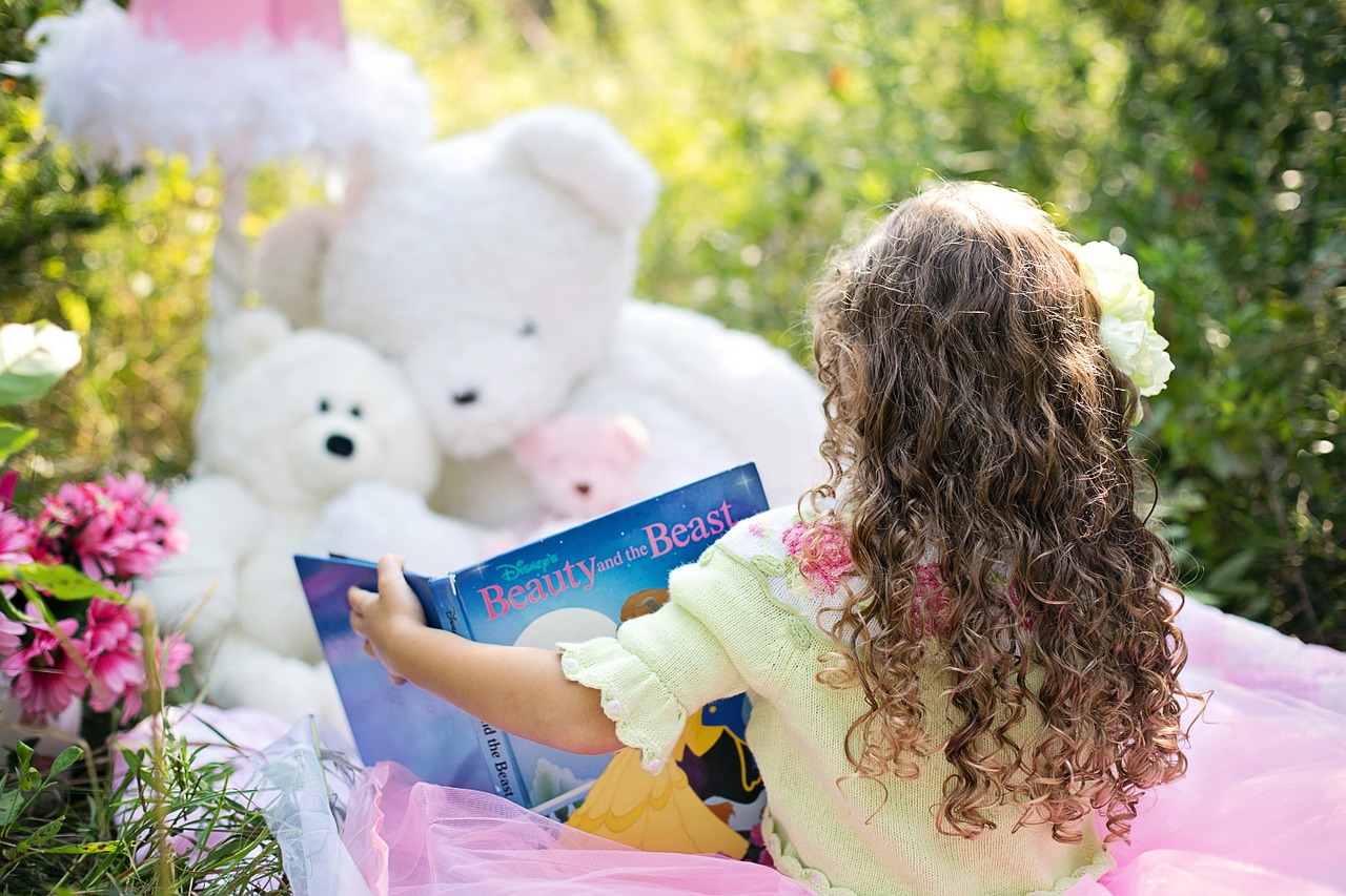A little girl reading to her stuffed bears in the summer time.