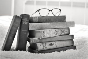 A black and white image of a stack of vintage books with a pair of glasses on top.