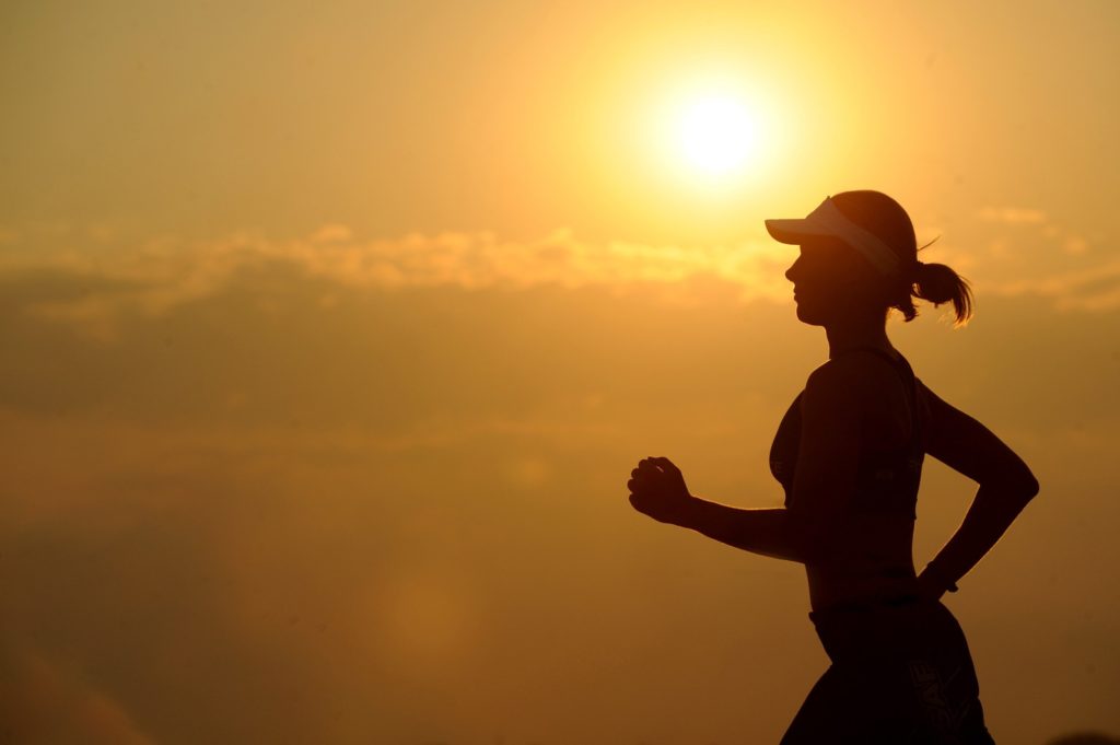 Image of a woman in a baseball cap running at sunrise